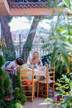 Vertical view of single mother having breakfast with two sons on lush family terrace in Spain