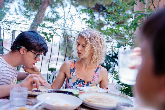Teenage son with Down syndrome leaning on single mother during quiet family breakfast in Spain
