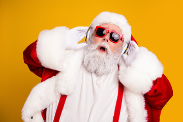 Naklejka premium Festive Santa Claus wearing red sunglasses and headphones enjoying Christmas music in a bright studio portrait