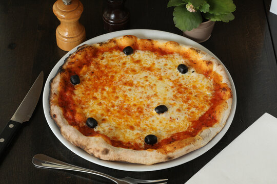 Pizza sur une assiette blanche avec des olives noires sur une table en bois