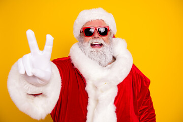 Naklejka premium Santa Claus wearing sunglasses and a red fur-trimmed suit flashing a peace sign and laughing on a bright yellow background for modern holiday cheer