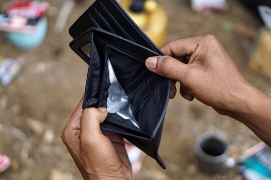 The concepts of financial crisis and poverty are illustrated by a close-up shot of a hand opening an empty black leather wallet containing no cash.