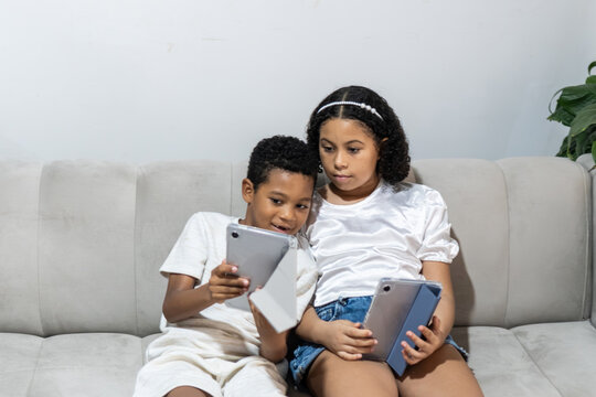 Children sitting on sofa using digital tablets