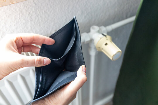 Hands holding an empty wallet in front of a heating radiator. Conceptual image of high energy bills and expensive utility costs.