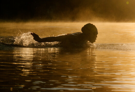 White swimmer performing stroke in open water with sunrise lighting