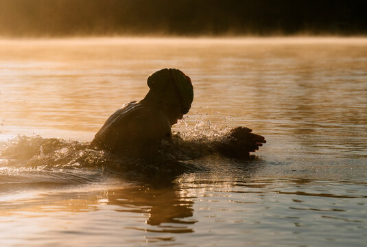 White swimmer practicing stroke in lake at early morning light