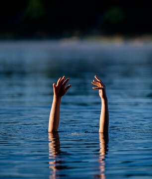 Two arms and hands reaching above calm lake water