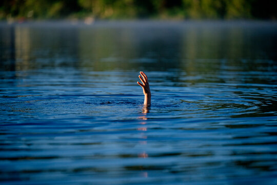 Hand reaching out of water as white person struggles to stay afloat