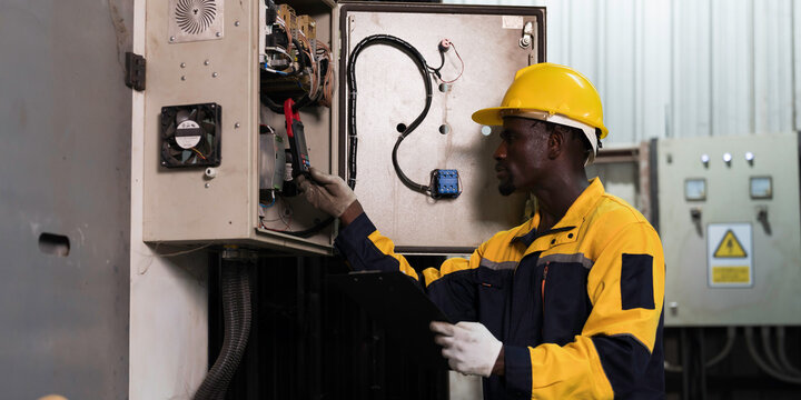 Electrician working on electrical control panel in factory. Professional electrician working, inspecting electrical panel. Male electrician checking electrical circuit board with safety uniform