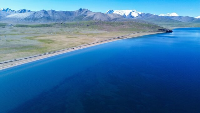 Aerial drone view of turquoise Lake Puma Yumco with snow-capped Kula Khangri Himalayan peaks and a coastal road in Nagarz&ecirc;, Tibet