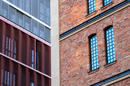 Historic brick facade beside modern red metal and glass architecture creates an urban contrast between old industrial character and new development