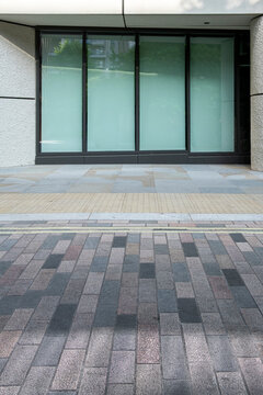 Modern building entrance with glass doors and patterned paving creates a clean geometric urban facade with simple contemporary architectural design