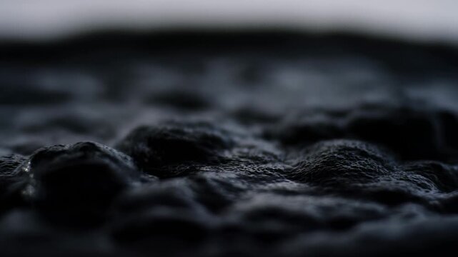 Dark liquid texture ripples across a shallow-focus abstract surface. Editorial design, dramatic transition.