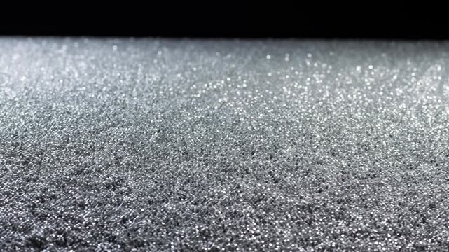 Shimmering granular texture sparkles across a silver metallic surface beneath a dark background. Luxury branding, fashion advertising, and jewelry promotion.
