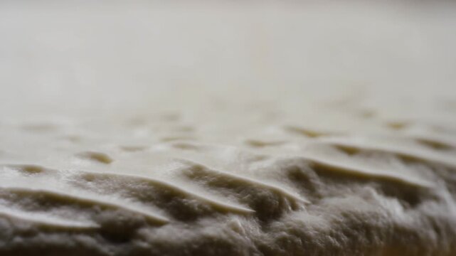 Raw bread dough is prepared on a wooden worktop in an extreme close-up bakery scene. Bakery advertising, bread-making tutorials, and baking education.