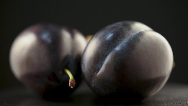 Purple whole and cut slice plums on black background