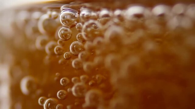 Carbonated amber beverage with bubbles rising inside a glass in macro close-up. Beverage advertising, soft drink promotion, and food and beverage campaigns.