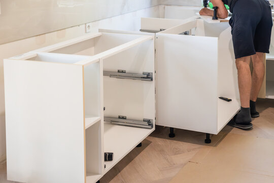 Worker assembling white kitchen base cabinets, cabinetry installation, kitchen renovation and home improvement.