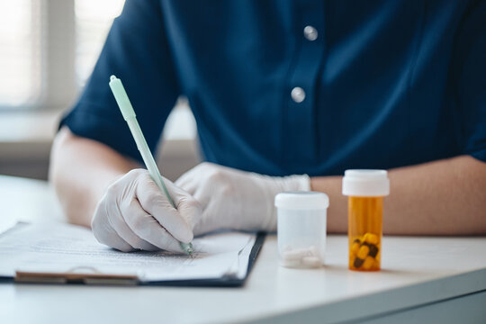 Caucasian doctor in protective gloves writing prescription on clipboard near medication bottles. Useful for pharmacy, medical insurance and healthcare advertising