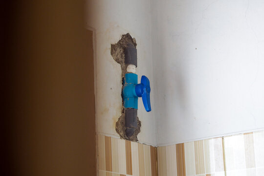 close-up view of a blue plastic water valve installed inside a damaged wall section exposed near tiled wall surfaces.
