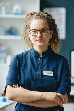 Vertical portrait of young adult Caucasian female veterinarian standing with crossed arms in clinic. Image suitable for pet healthcare advertising and veterinary services promotion