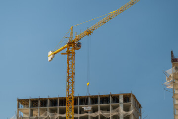 Construction crane towers over a new building rising against a clear blue sky during a warm afternoon © beholdereye