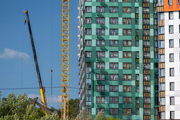Construction progress of a modern residential building with cranes and colorful facades on a sunny day © beholdereye