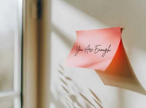 Encouraging pink sticky note with positive message on wall near window