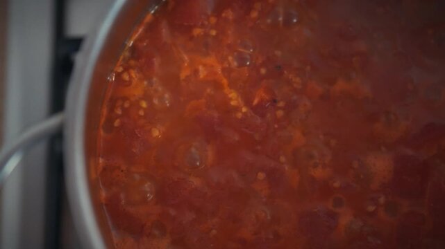 Homemade tomato sauce simmering in a metal pot. Top view close-up shows tomato pulp and active bubbles on the surface. Concept of pizza sauce preparation and organic home cooking