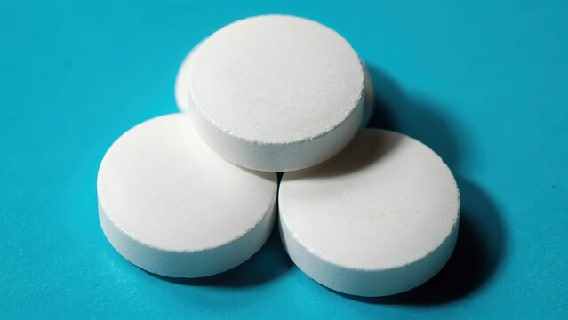 Three large white round tablets arranged in a triangle on a blue background with medicine medication pharmaceutic