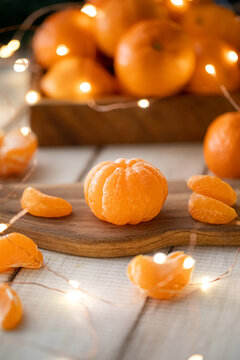 Fresh juicy peeled mandarin orange with slices on small wooden cutting board with warm glowing christmas lights