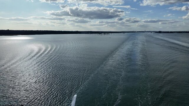 The view from the top deck of a cruise ship sailing away from the port and city of Southampton, England. The wake of the ship is in clear view, and the aft of the ship is visible at the end.