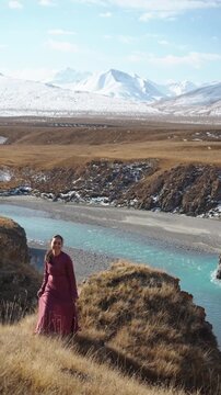 Asian Woman in Traditional Dress on Cliff Overlooking Turquoise River in Sary Jaz Valley Kyrgyzstan