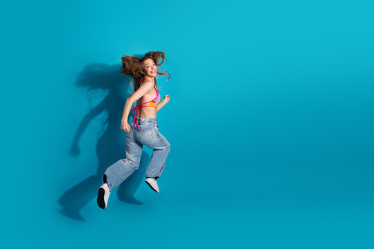 Positive woman in colorful casual wear jumping energetically on a blue background expressing joy and liveliness