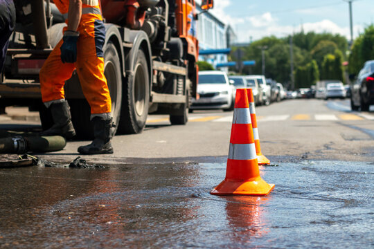 A road construction crew is working on the road; a traffic cone is placed nearby.