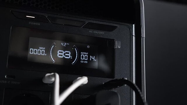 Portable power station for powering devices via multiple connected cables; display showing battery charge percentage and output power. Concept of backup power and energy independence; electricity