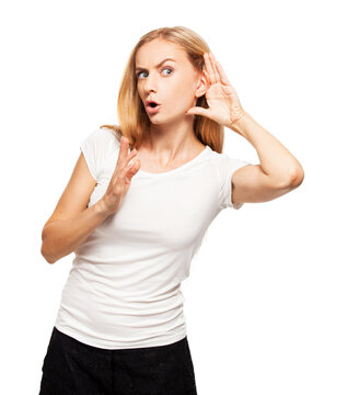 Surprised young woman listening with hand near ear and holding palm up. Blonde girl in white t-shirt eavesdropping on gossip isolated on white background.