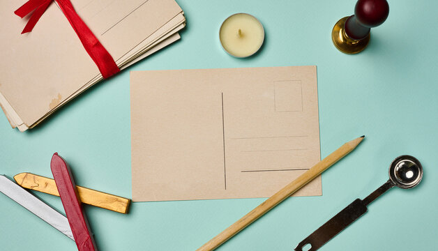 Vintage postcard, stack of letters with a red ribbon, candle, pencil, and wax seal on a turquoise background