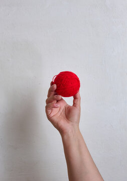 A person holding a red ball of wool yarn in their hand against a light textured background.