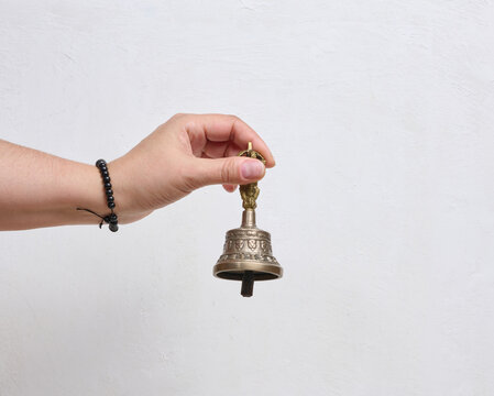 A person holding a traditional Tibetan bronze bell in their hand against a white background.