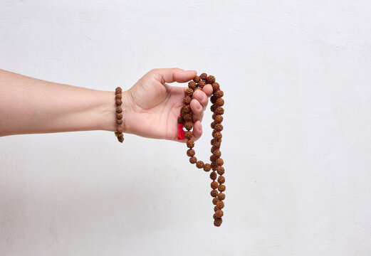 A person holding rudraksha prayer beads in their hand against a light background.