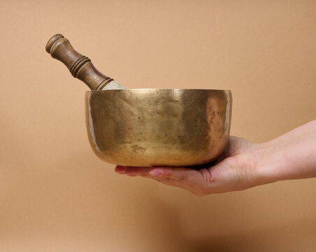 A copper singing bowl and a wooden mallet in a woman's hand