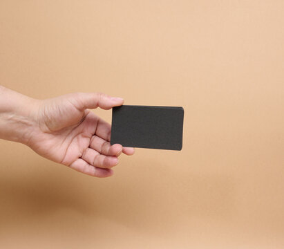 A person holding a stack of black business cards against a beige background.