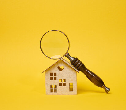 Magnifying glass with a wooden handle lying on a decorative toy house on a bright yellow background.