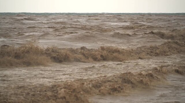 Brown muddy waves churn at a river mouth where floodwater meets the sea after heavy rain.