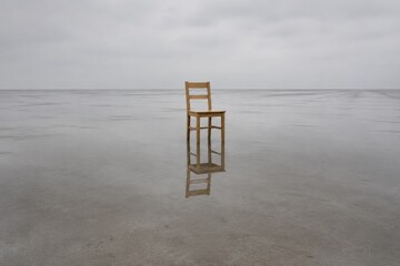 Obraz premium Single wooden chair standing in a wide shallow sheet of rainwater