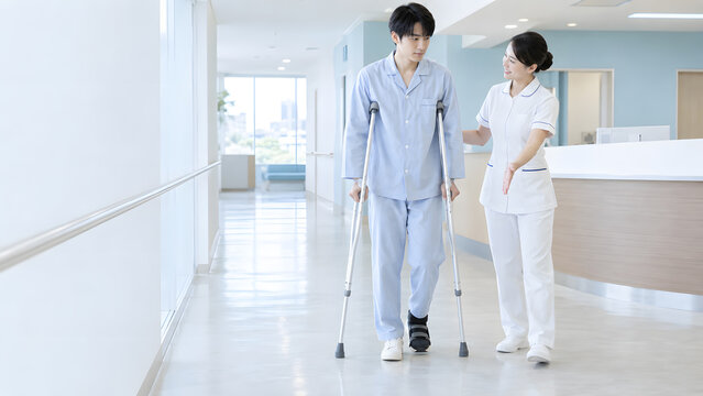 病院の廊下で松葉杖を使って歩行訓練する若い男性患者と女性看護師