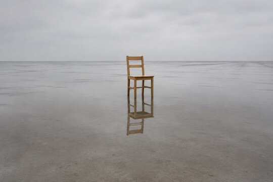 Single wooden chair standing in a wide shallow sheet of rainwater