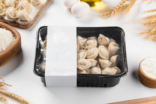 Uncooked frozen meat dumplings pelmeni in plastic tray packaging with blank label mockup on floured table