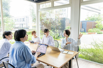 Obraz premium 緑が見える明るいオフィスで会議をする5人の日本人ビジネスチーム